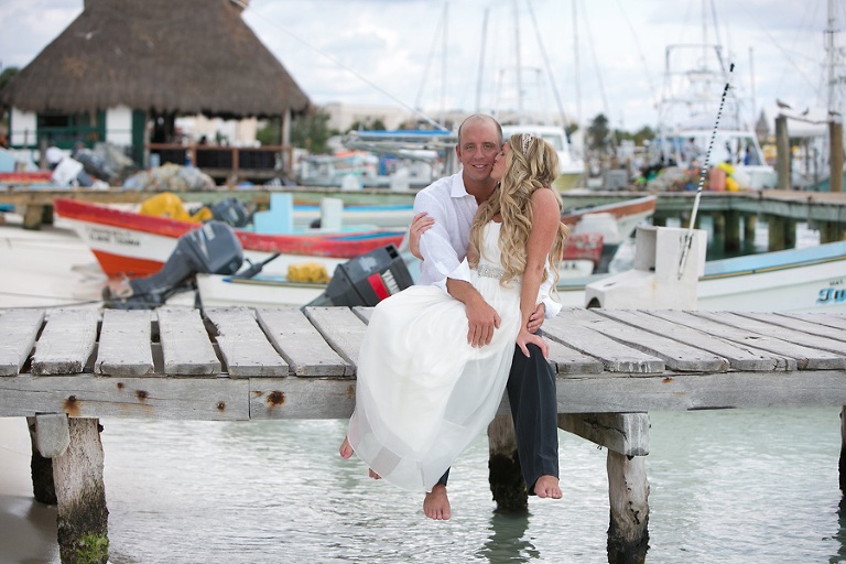Bride sitting on groom's lap on dock in Mexico